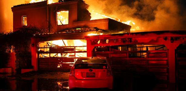 Fumaça e chamas sobem de uma casa em chamas, enquanto ventos fortes alimentam incêndios florestais devastadores na área de Los Angeles e forçam as pessoas a evacuar, em Malibu, Califórnia, EUA, 8 de janeiro de 2025
