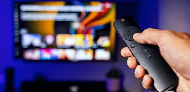 Homem segurando controle remoto apontando para TV em segundo plano; tv 3.0, smartv